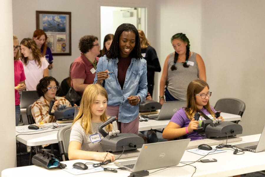 Three participant smiling and using the flight simulators while people look on in the background